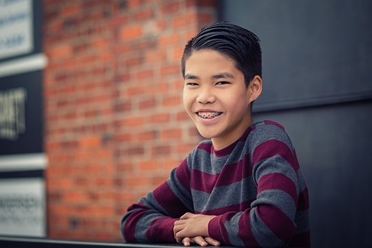 Happy smiling teenage asian boy with braces leaning over outdoor railing.